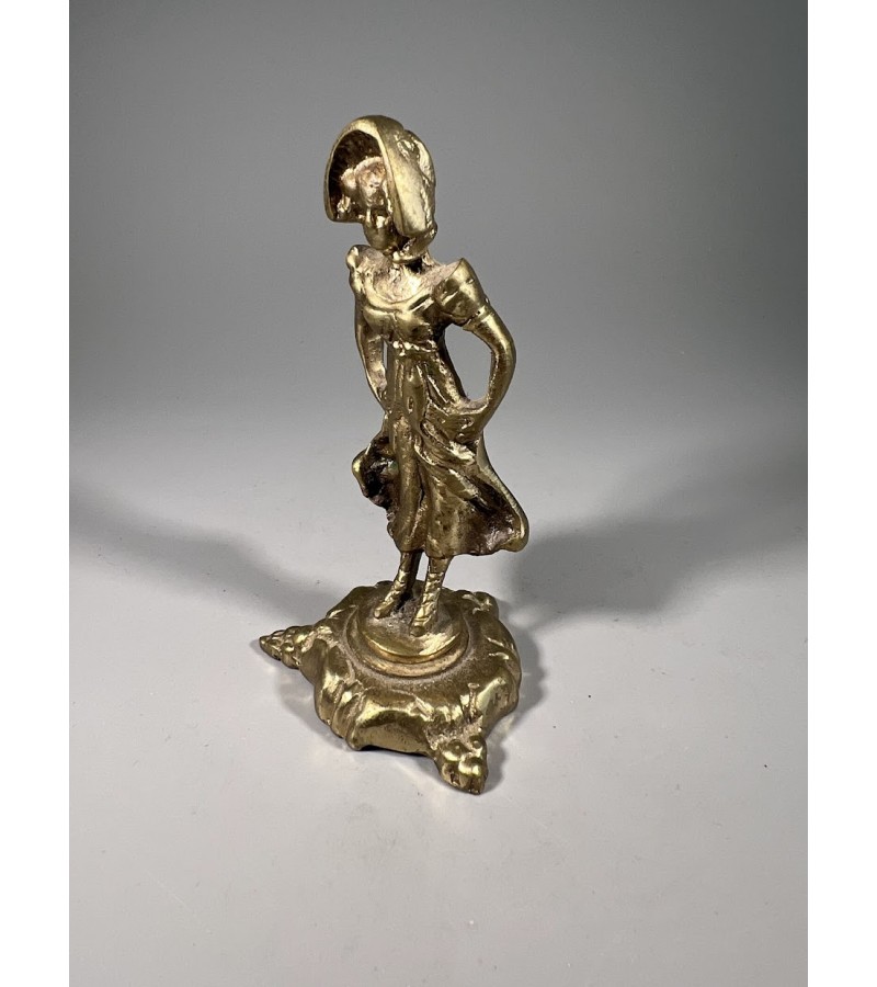 Statulėlė žalvarinė Stovinti moteris, vilkinti XVIII a. pabaigos ar XIX a. apranga, su plačiabryle kepuraite ir laisvai krintančia suknele. Kaina 23