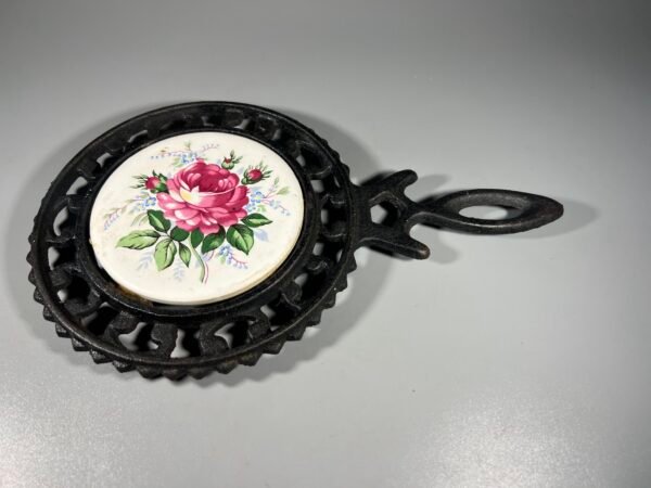 Padėklas ketaus, špižinis karštam indui padėti, su keramikos plytele, dekoruota rožių motyvu. Kaina 18