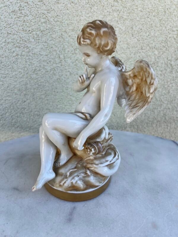 Statulėlė, skulptūrėlė Sėdintis kupidonas, pagal Etienne-Maurice Falconet (1716–1791) skulptūrą. Prancūzija, Vokietija. Porcelianas, monochrominė tapyba, auksavimas. XIX a. pr. Kaina 83